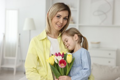 Photo of Little daughter congratulating her mom with bouquet of tulips at home. Happy Mother's Day
