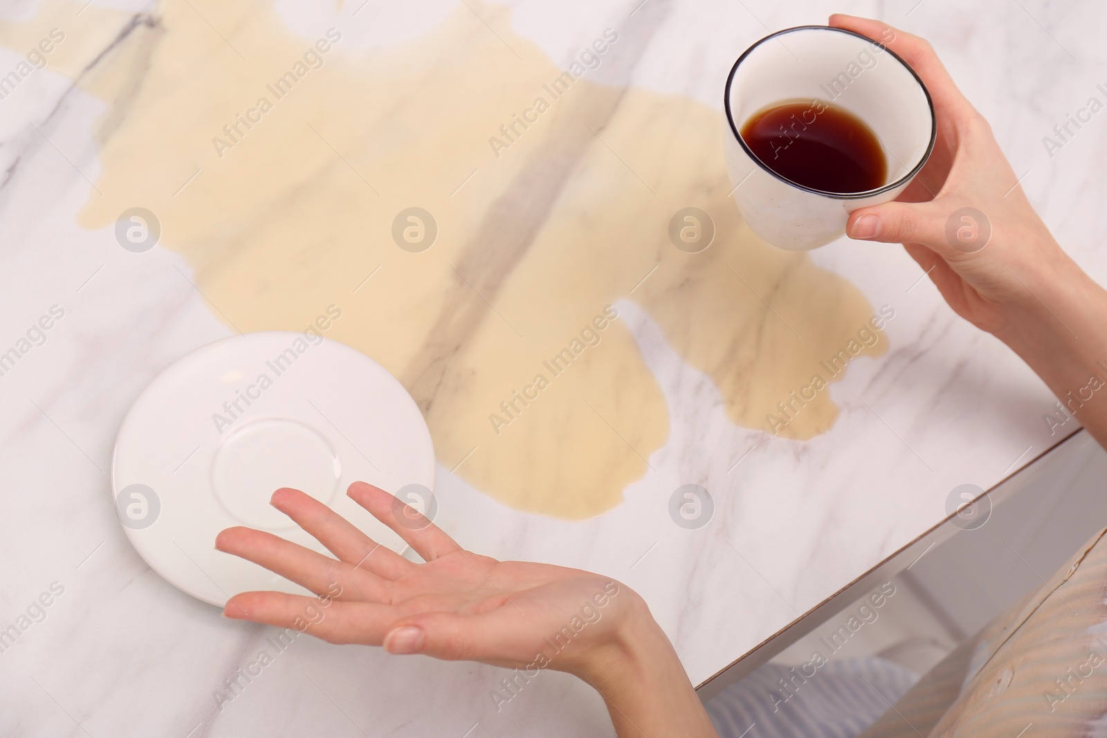 Photo of Woman holding cup near spot of coffee at marble table, closeup