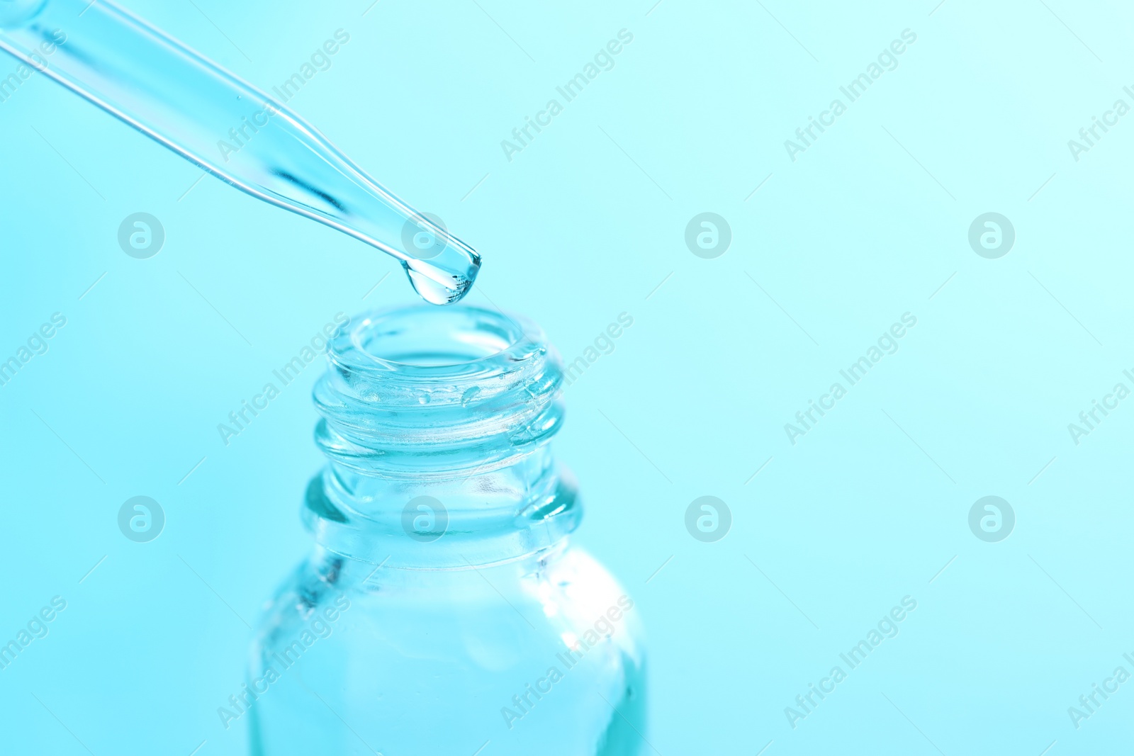 Photo of Dripping liquid from pipette into glass bottle on light blue background, closeup. Space for text