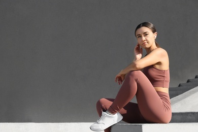 Photo of Young woman in stylish sports wear sitting on stone parapet. Space for text