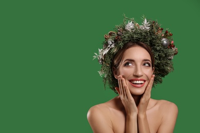 Emotional young woman wearing Christmas wreath on green background. Space for text