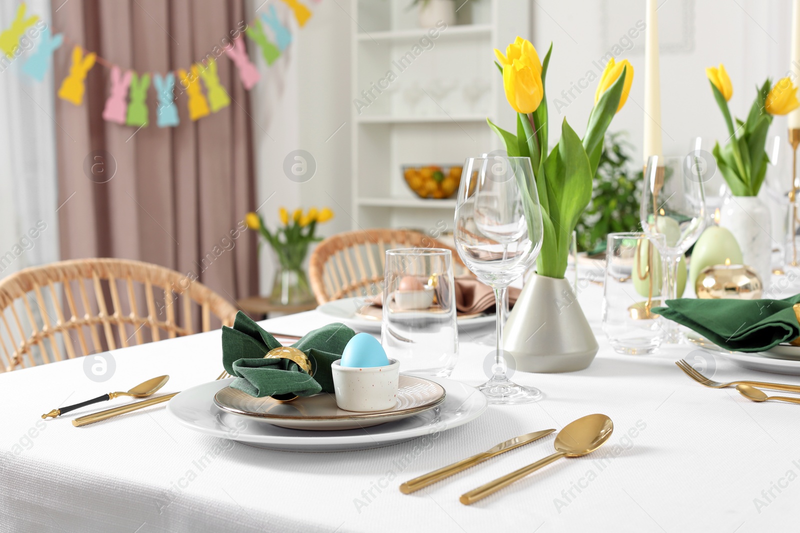 Photo of Festive Easter table setting with painted eggs, burning candles and yellow tulips in room