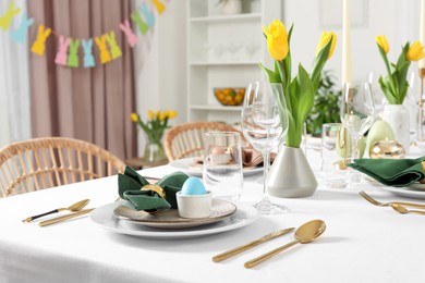 Photo of Festive Easter table setting with painted eggs, burning candles and yellow tulips in room