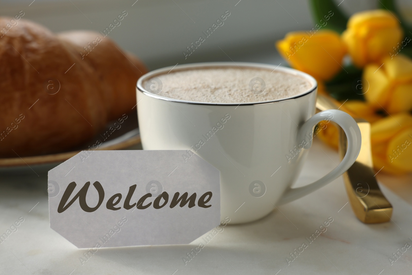 Image of Welcome card, cup of aromatic coffee and croissant on tray and beautiful yellow tulips