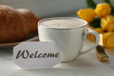 Welcome card, cup of aromatic coffee and croissant on tray and beautiful yellow tulips