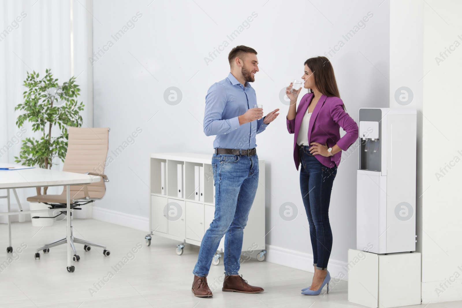 Photo of Employees having break near water cooler in office. Space for text