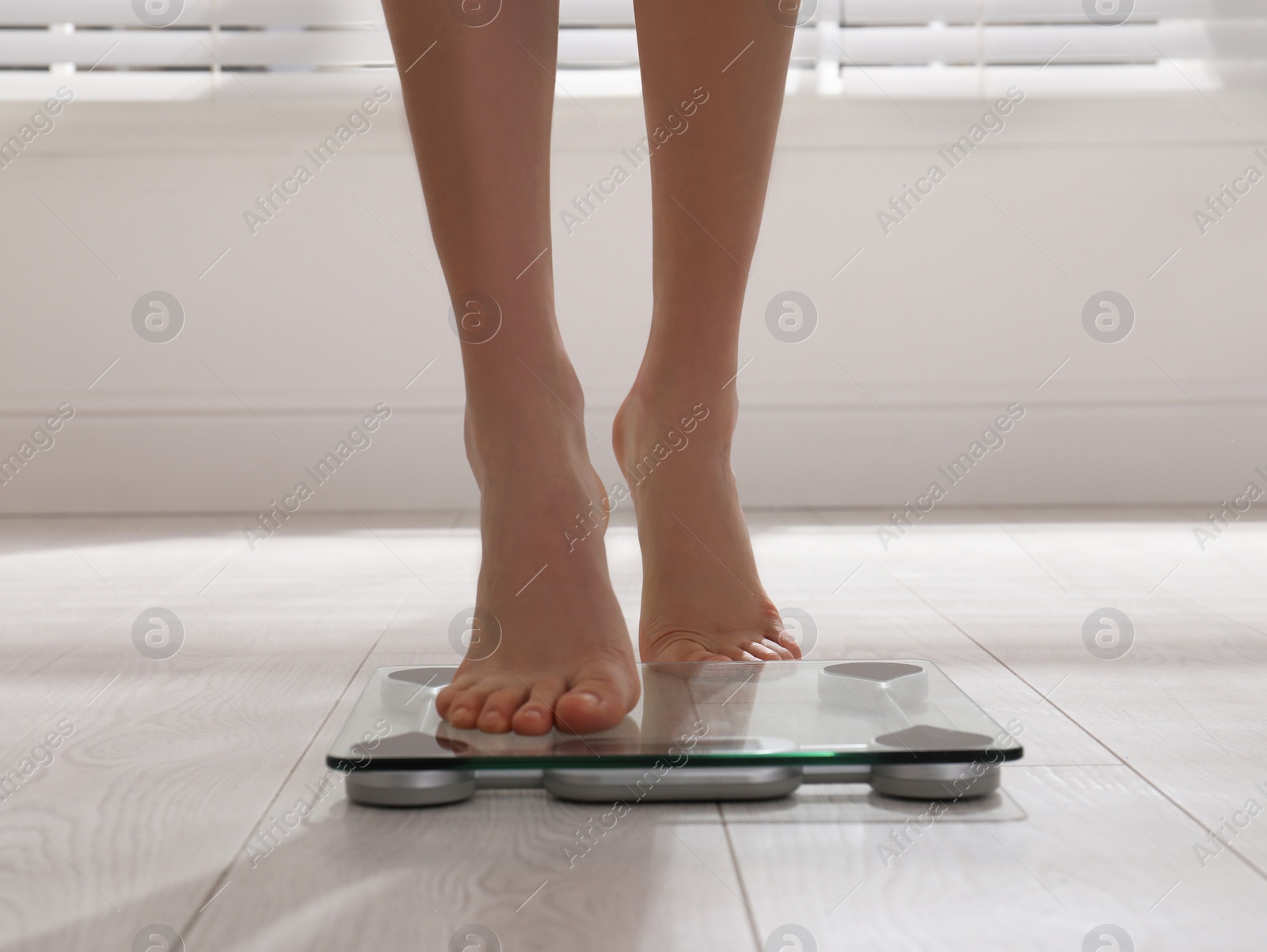 Photo of Woman stepping on floor scales indoors, closeup. Weight control