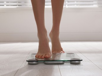 Woman stepping on floor scales indoors, closeup. Weight control