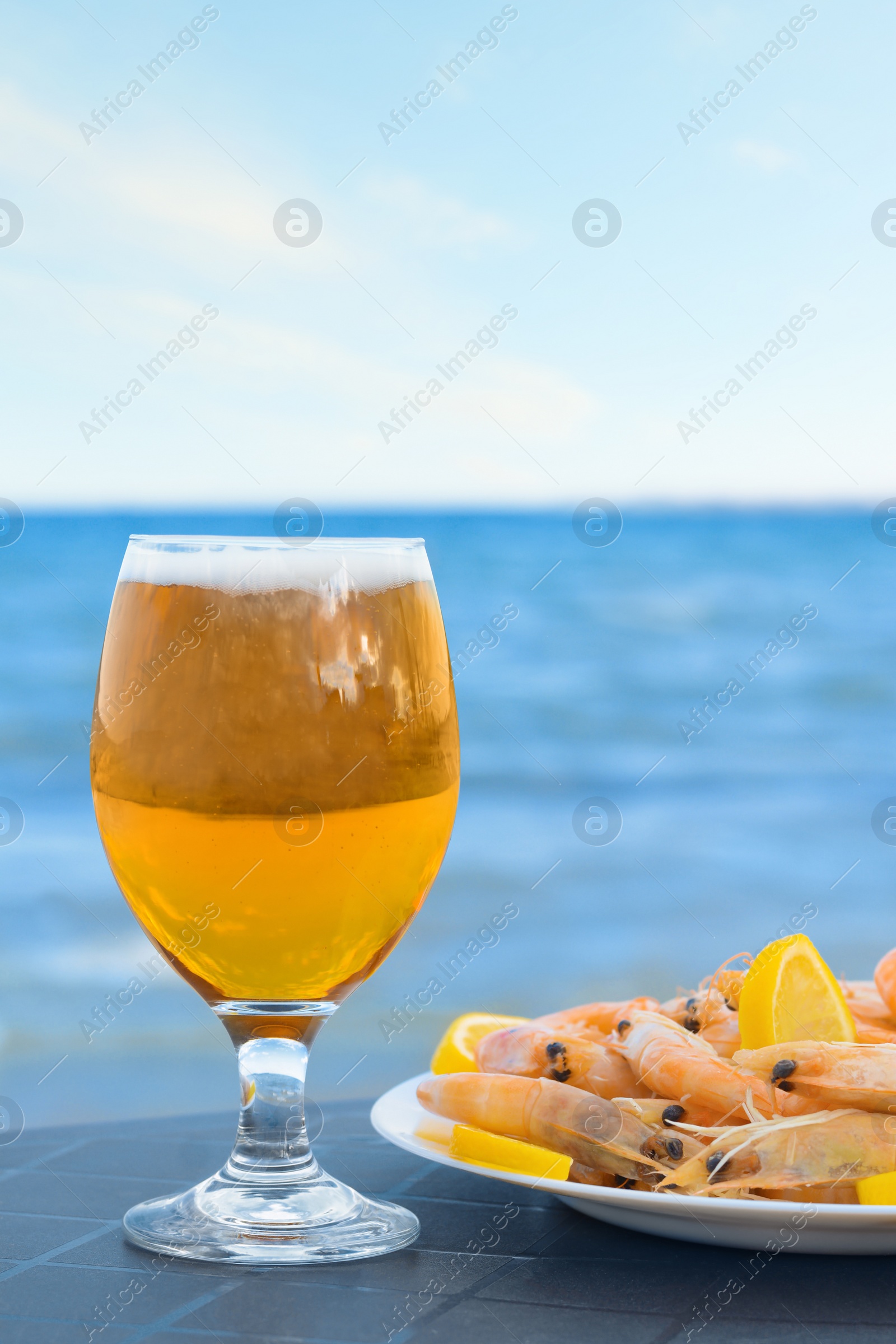 Photo of Cold beer in glass and shrimps served with lemon on beach