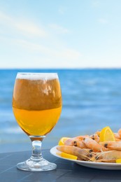 Cold beer in glass and shrimps served with lemon on beach