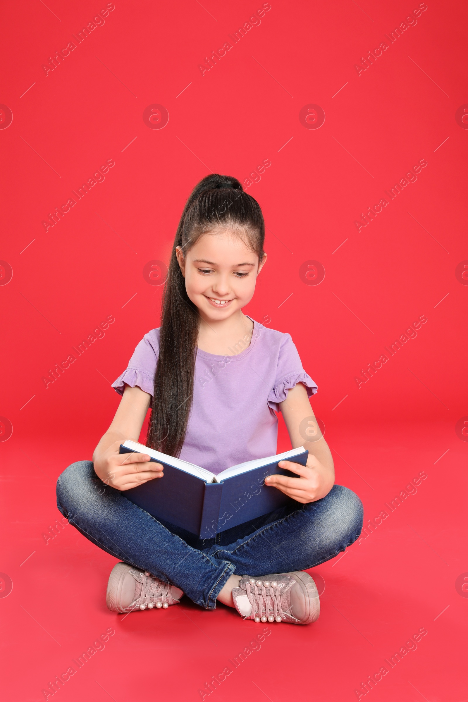 Photo of Cute little girl reading book on color background, space for text