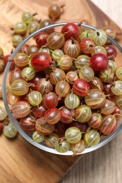 Photo of Glass bowl with fresh ripe gooseberries on wooden table, flat lay