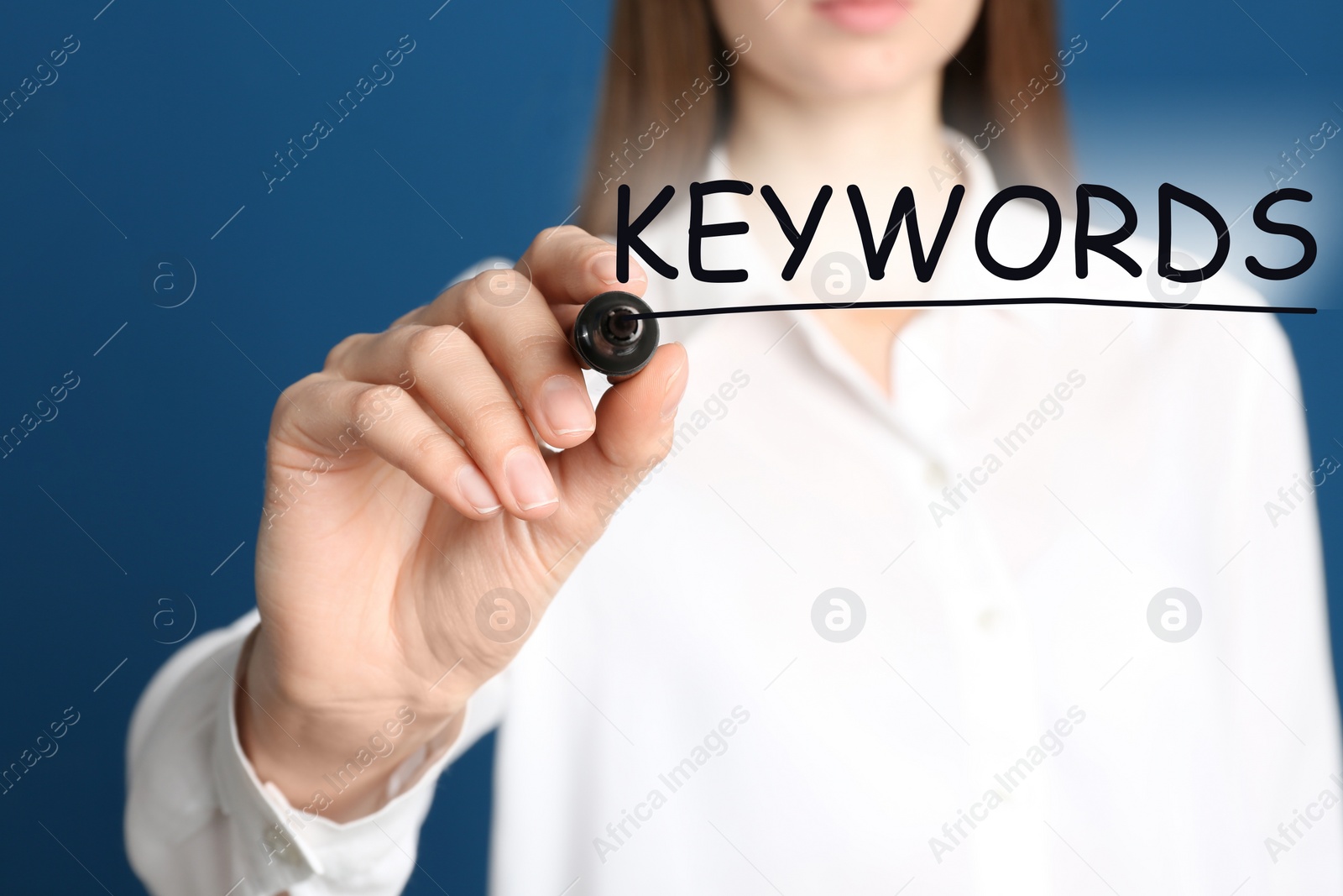 Image of Woman writing word KEYWORDS on transparent board against blue background, closeup