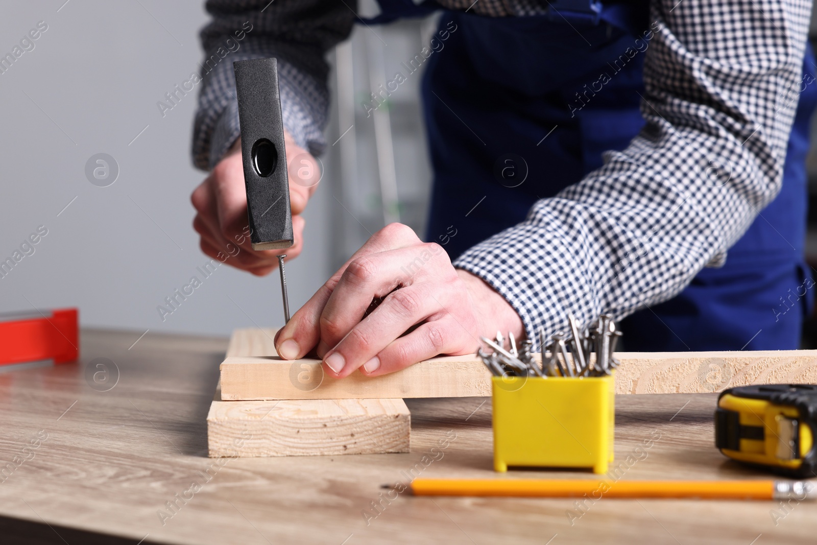 Photo of Professional repairman hammering nail into board at wooden table indoors, closeup