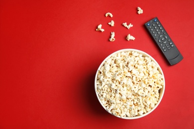 Bowl with popcorn, TV remote and space for text on color background, top view. Watching cinema