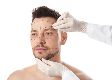 Photo of Doctor examining man's face before plastic surgery operation on white background