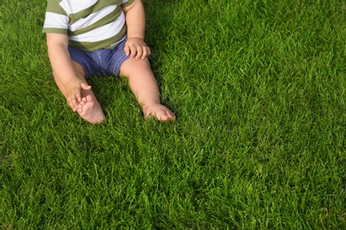 Photo of Adorable little baby sitting on green grass outdoors, closeup