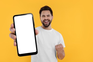 Happy man holding smartphone with empty screen on orange background