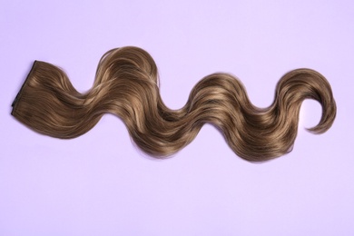 Photo of Lock of brown wavy hair on color background, top view