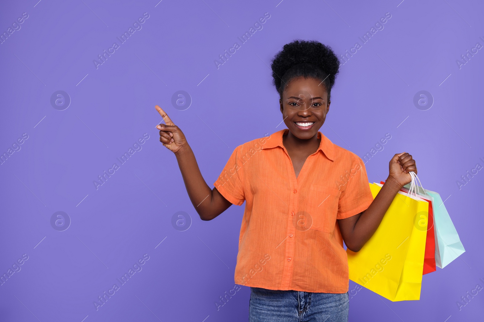 Photo of Happy young woman with shopping bags pointing at something on purple background. Space for text