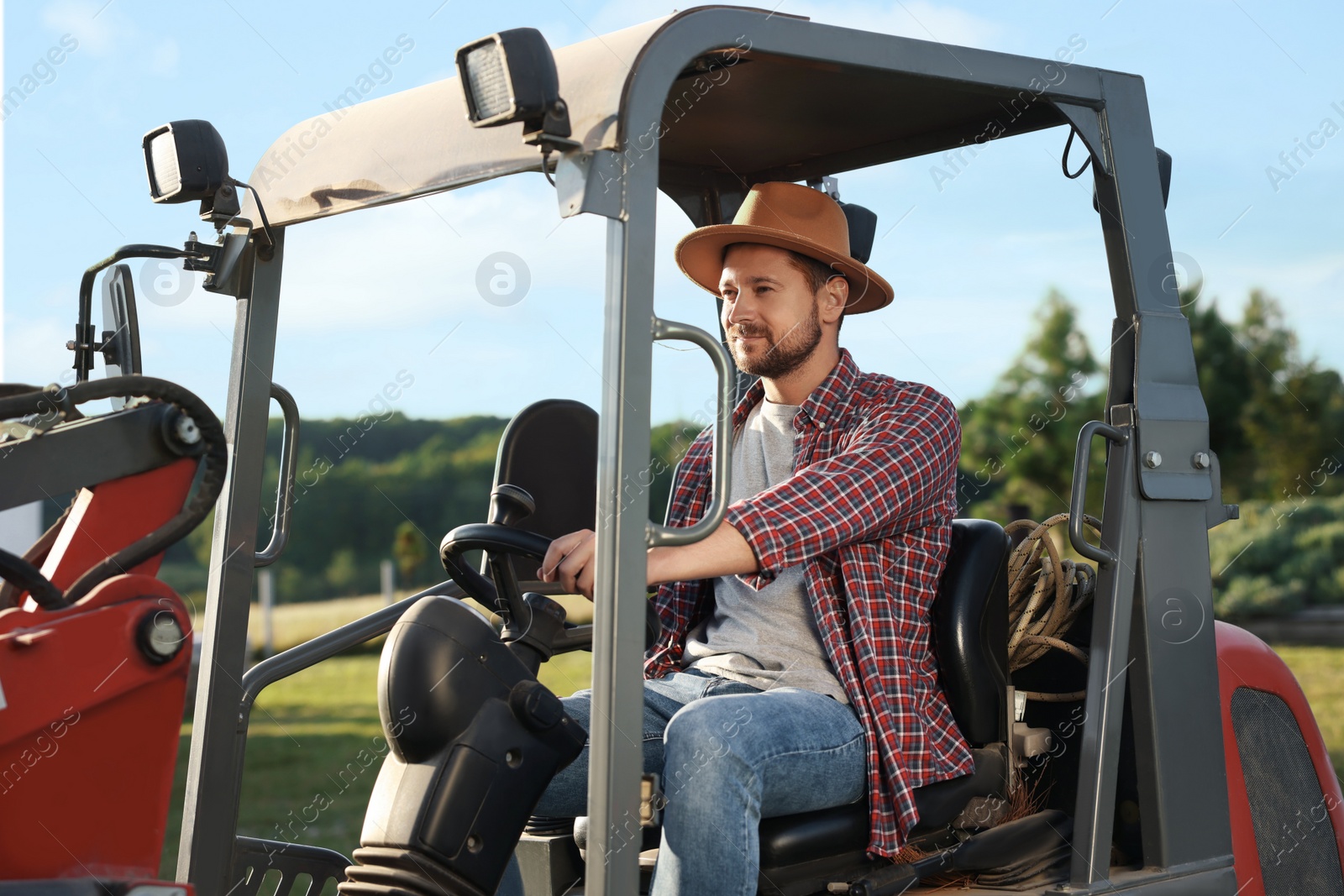 Photo of Farmer in hat driving loader outdoors. Agriculture equipment