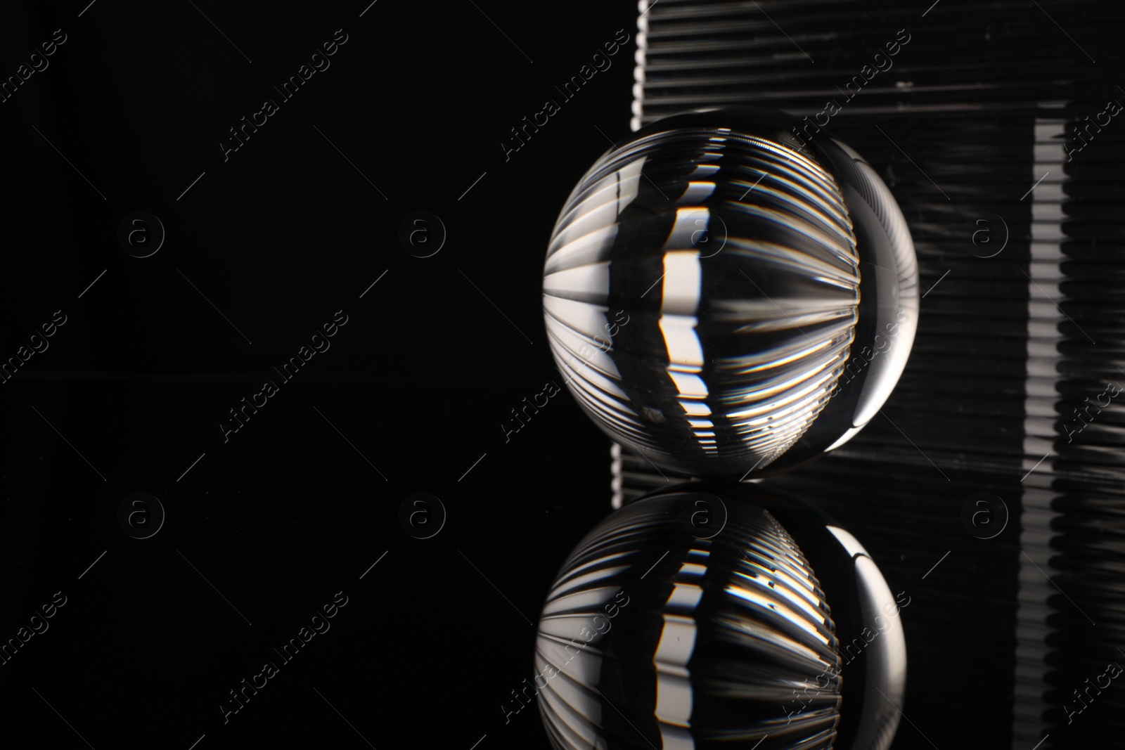 Photo of Transparent glass ball on black mirror surface. Space for text