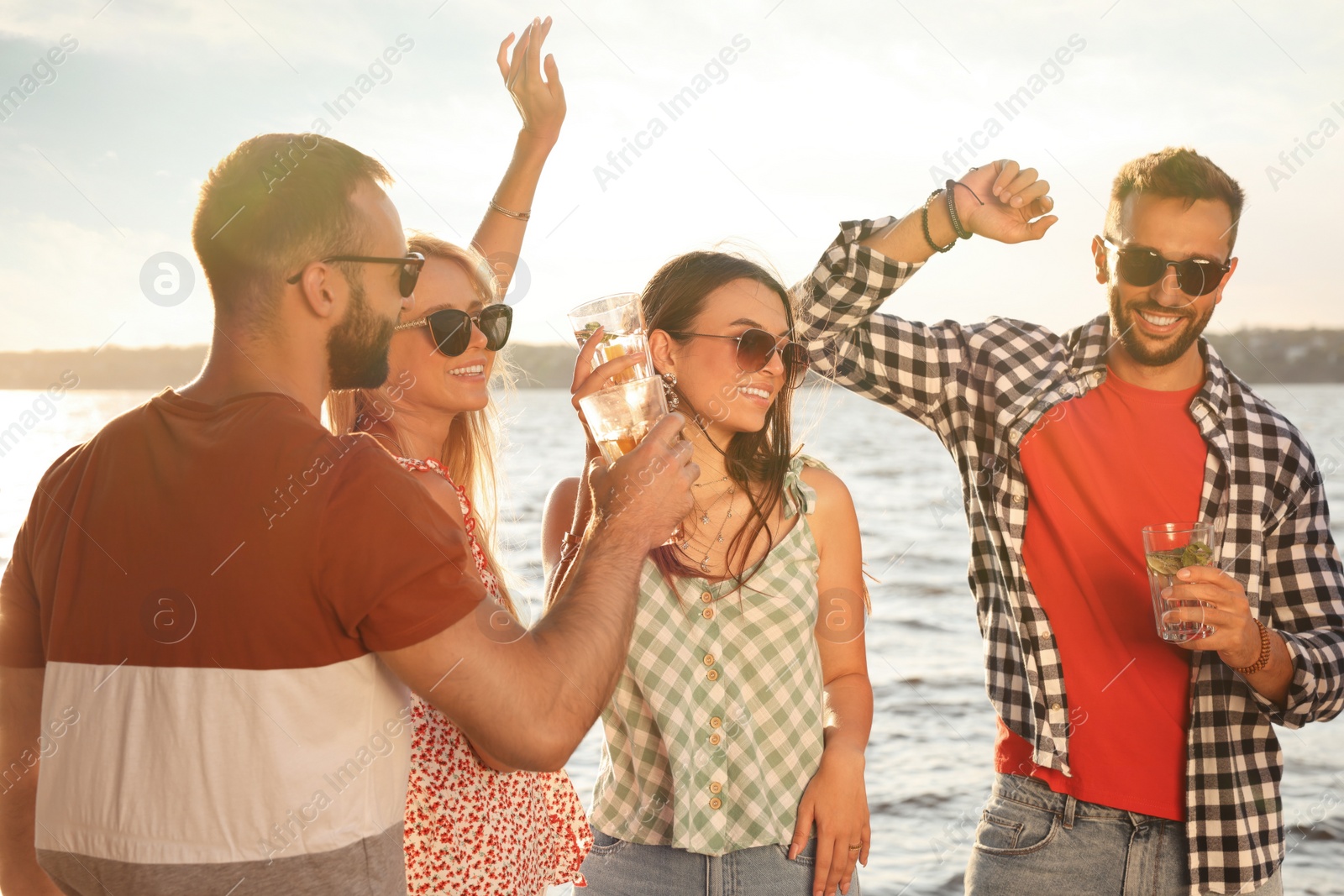 Photo of Group of friends with drinks having fun near river at summer party