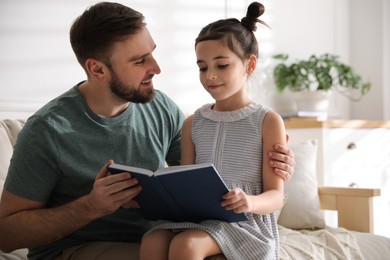 Photo of Little girl with father reading fairy tale in living room