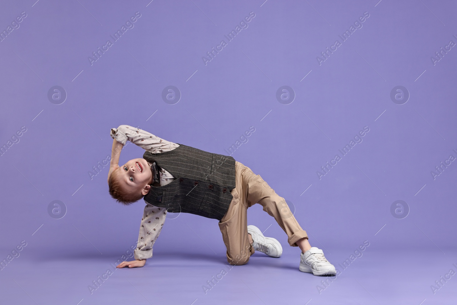 Photo of Happy little boy dancing on violet background. Space for text