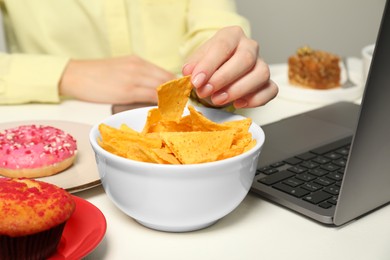 Photo of Bad habits. Woman eating tortilla chips at white office table, closeup