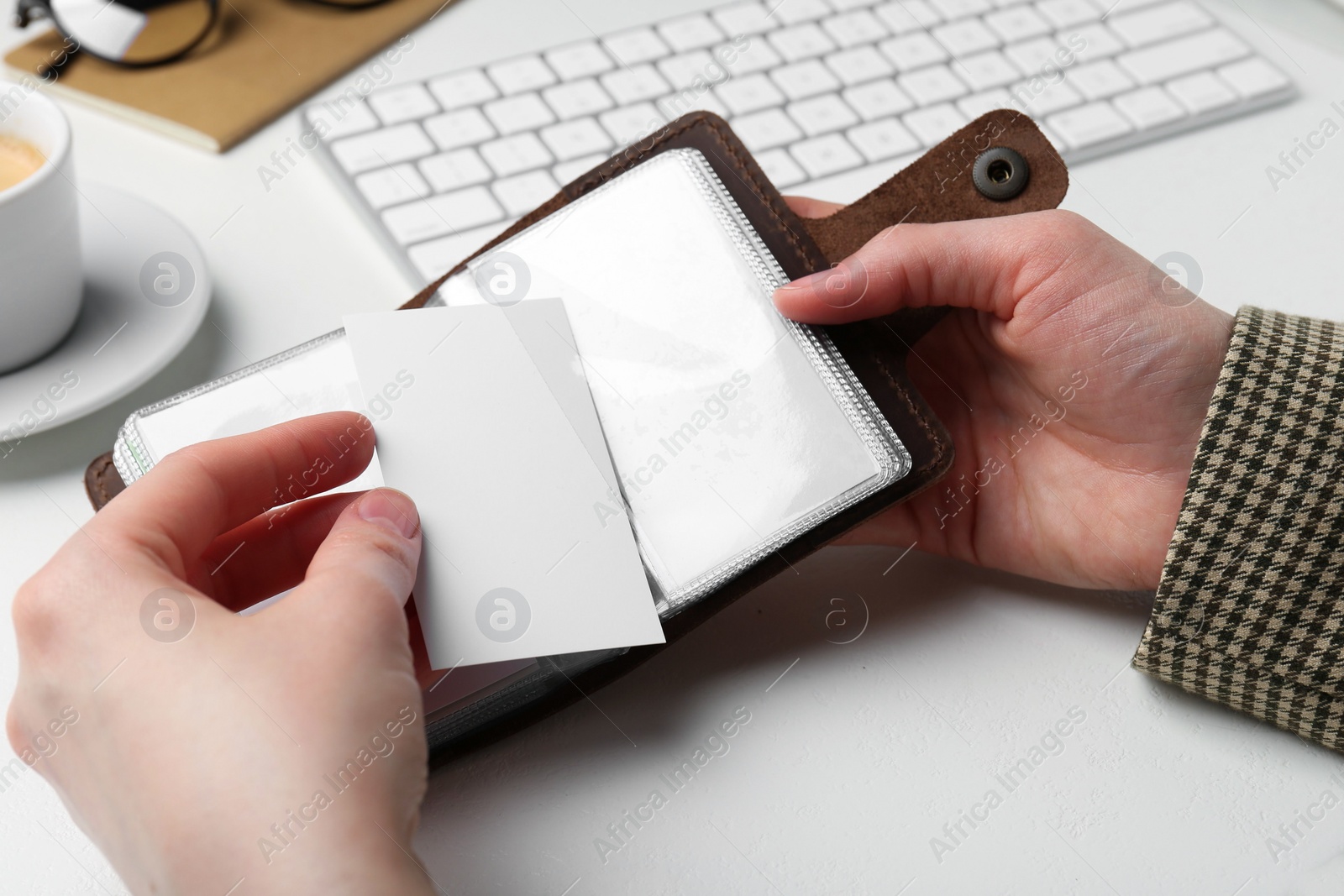 Photo of Woman holding leather business card holder with blank cards at white table, closeup