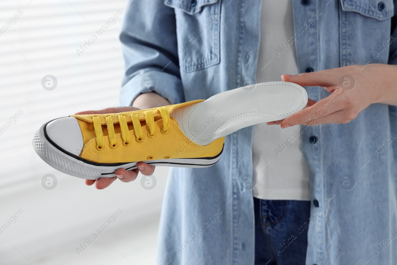 Photo of Woman putting orthopedic insole into shoe indoors, closeup. Foot care