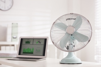 Photo of Modern electric fan and laptop on table in office