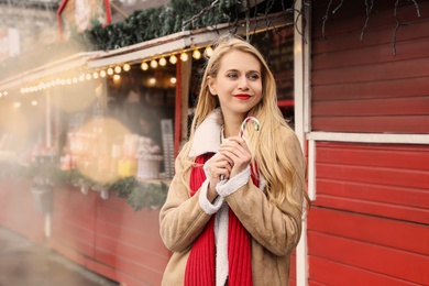 Photo of Young woman with candy cane spending time at Christmas fair