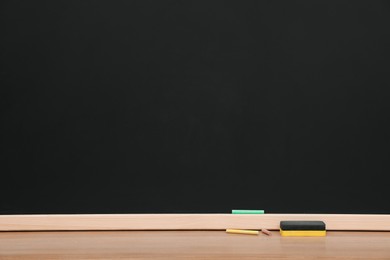 Colorful chalks and duster on wooden table near black board. Space for text