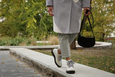 Stylish woman with trendy black baguette bag in park, closeup