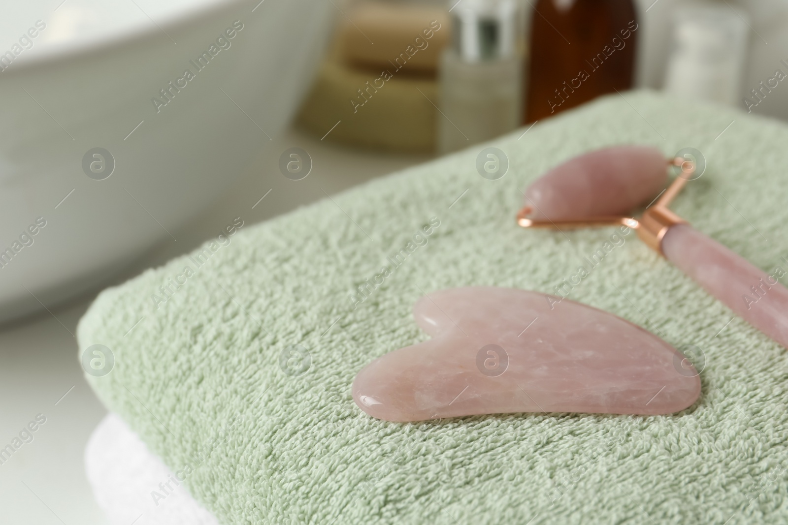 Photo of Rose quartz gua sha tool and natural face roller on towel in bathroom, closeup