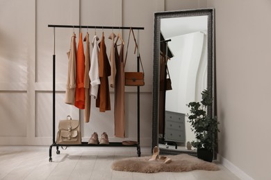 Photo of Rack with stylish women's clothes and mirror in dressing room