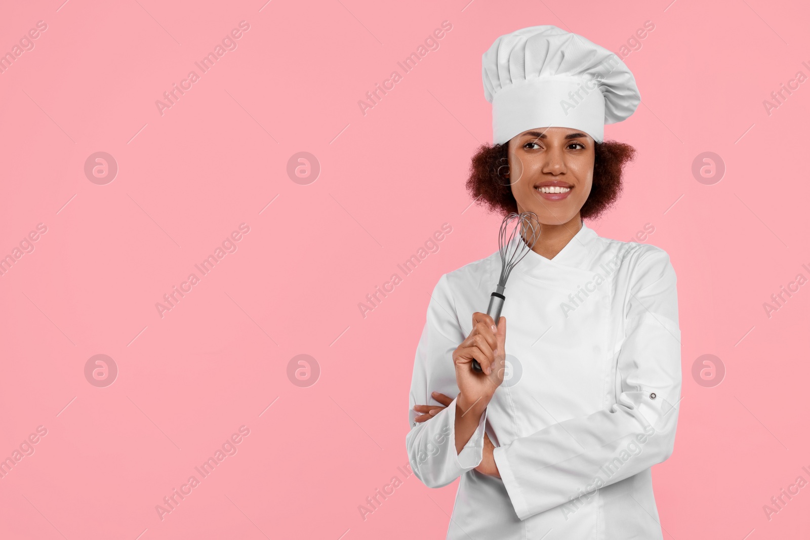 Photo of Happy female chef in uniform holding whisk on pink background. Space for text