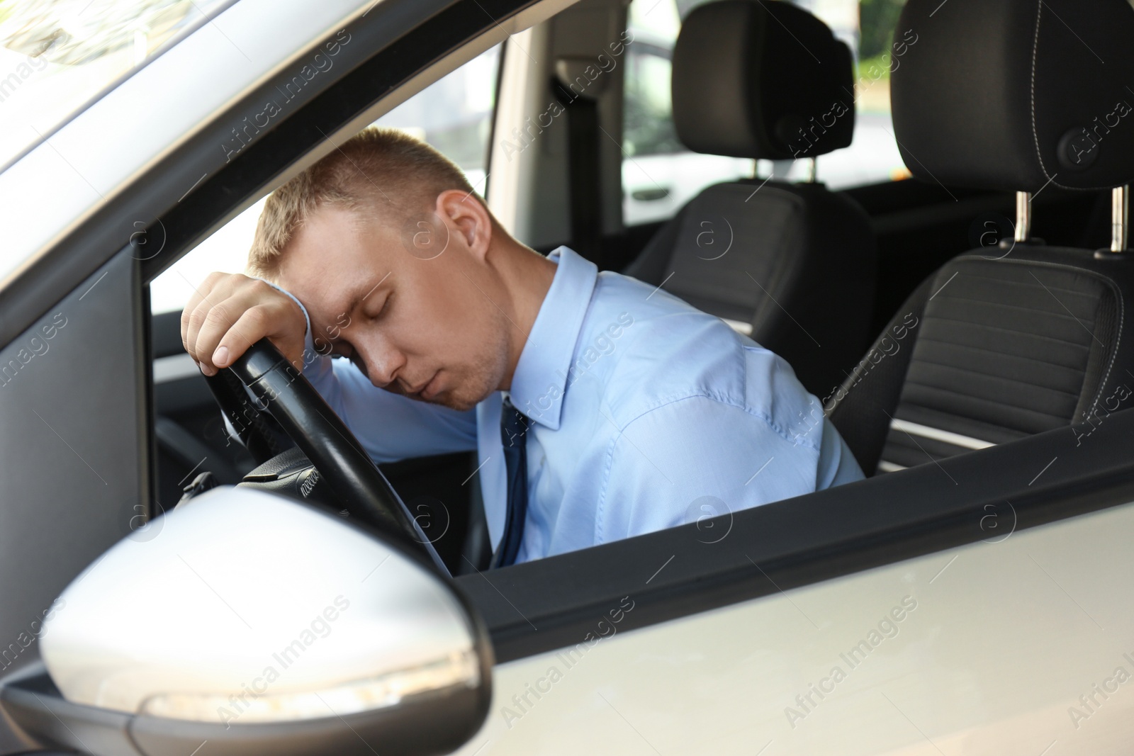 Photo of Tired young man sleeping on steering wheel in his car