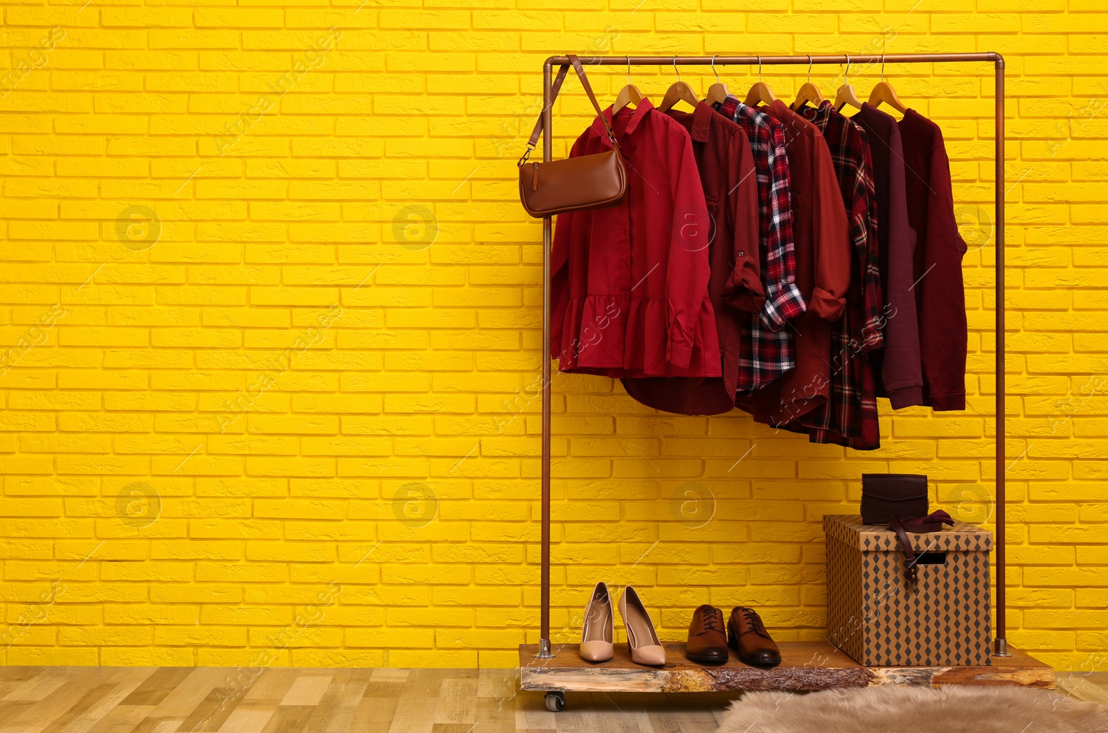 Photo of Rack with stylish clothes and bag near yellow brick wall indoors, space for text