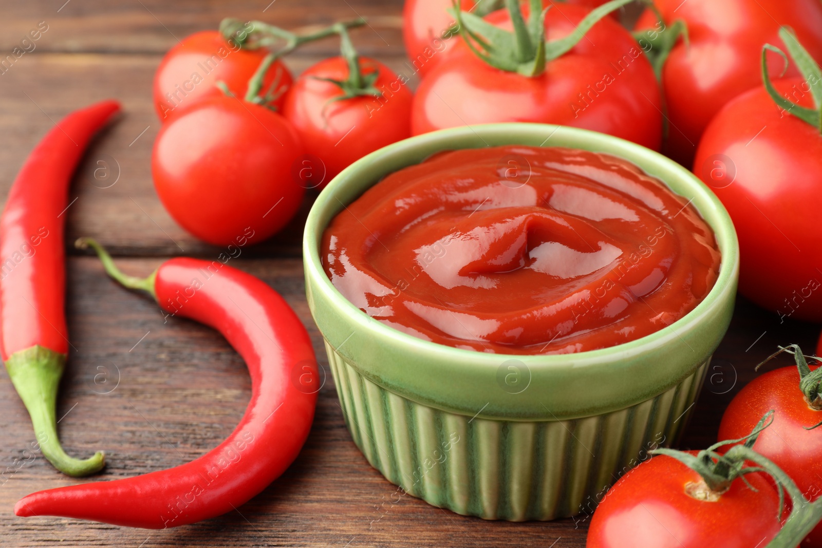 Photo of Bowl of tasty ketchup, chili peppers and tomatoes on wooden table, closeup