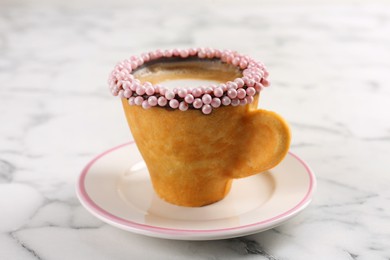 Photo of Delicious edible biscuit cup of coffee decorated with sprinkles on white marble table