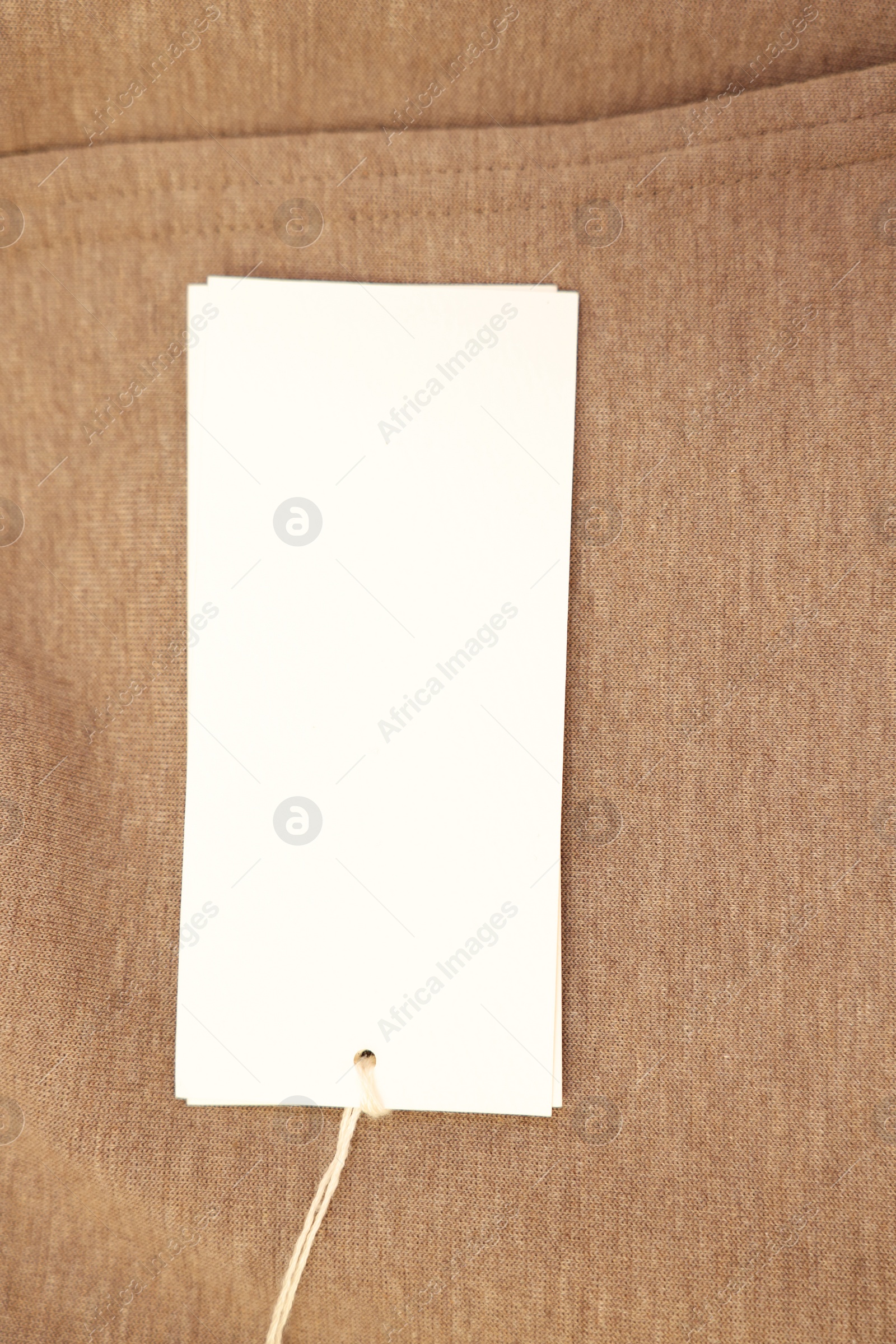 Photo of Cardboard tag on brown garment, top view. Space for text