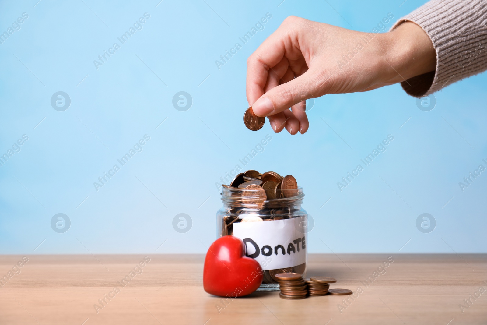 Photo of Woman putting coin into jar with label DONATE on table against color background, closeup. Space for text
