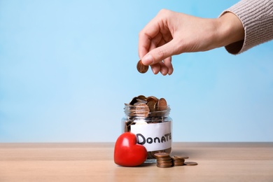 Photo of Woman putting coin into jar with label DONATE on table against color background, closeup. Space for text
