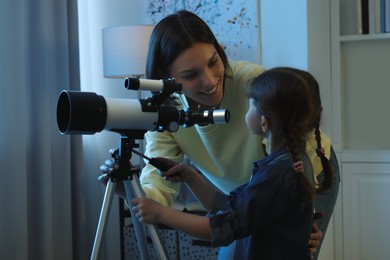 Photo of Happy mother and her cute daughter using telescope to look at stars in room