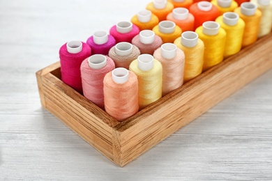 Photo of Container with set of color sewing threads on wooden background