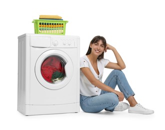 Photo of Beautiful woman sitting near washing machine with laundry on white background