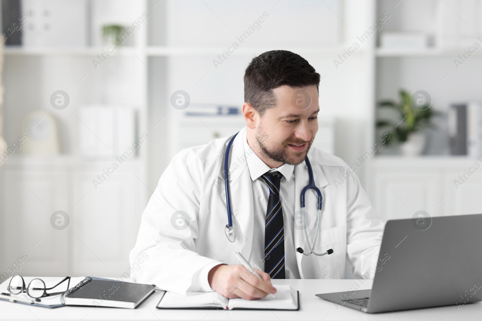 Photo of Doctor having online consultation via laptop at table in clinic